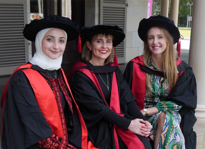 Three female phd graduates smiling towards the camera, wearing their graduation attire