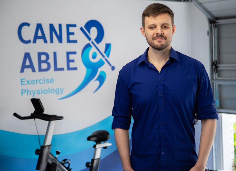 James Steggell looking directly to camera from his clinic. Cane and Able Logo in the background.