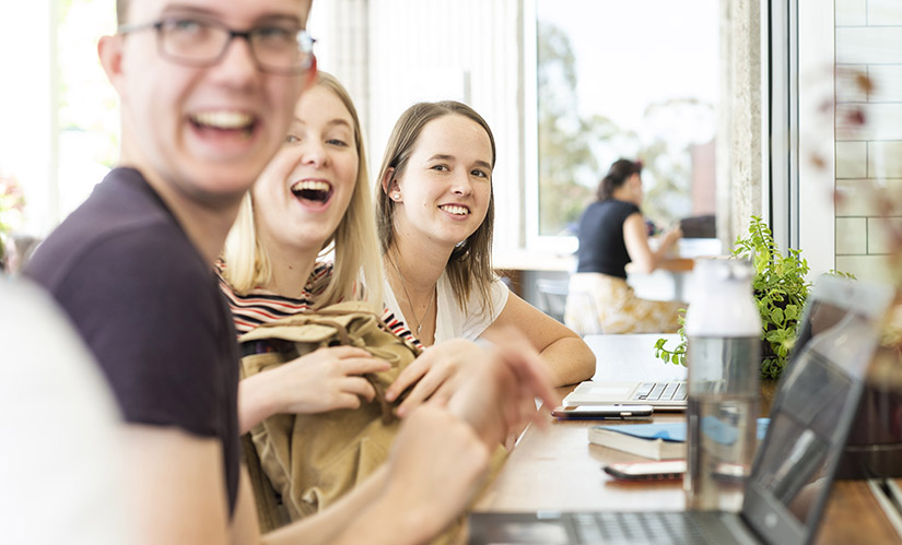 A group of laughing students sits at a cafe.