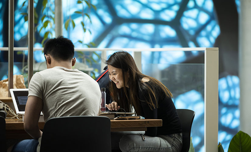 Two students are studying in a library space surrounded by plants, snacks and coffee.