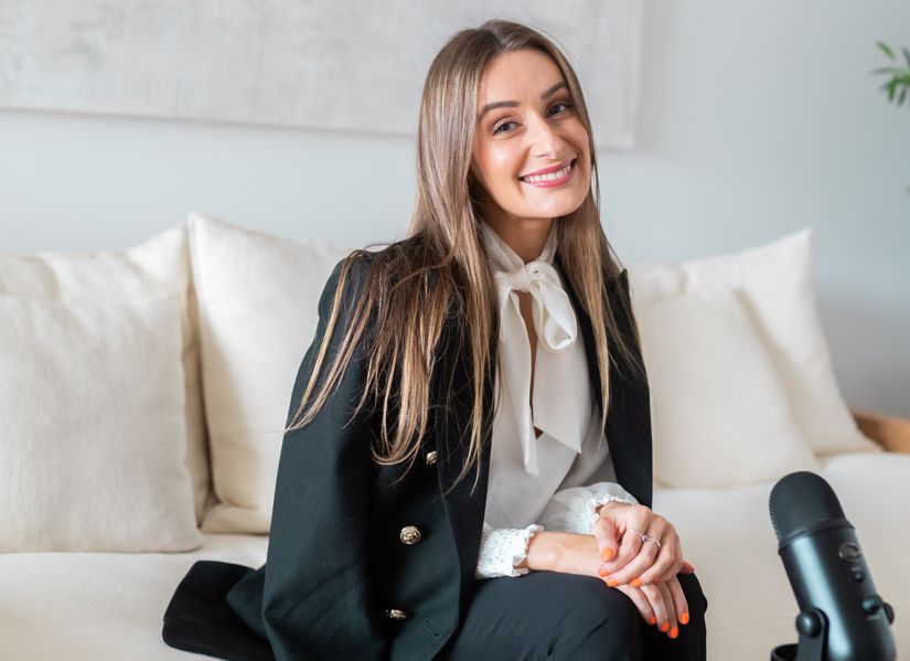 Amber Lowther seated smiling at camera with a microphone.