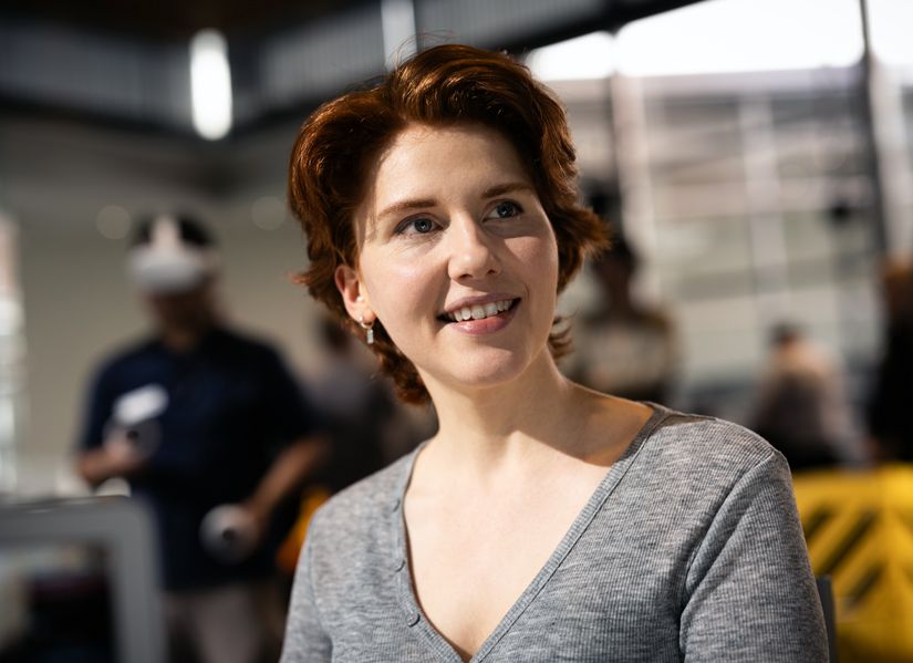 Young woman with red hair wearing gray top is smiling at someone to the right of the camera