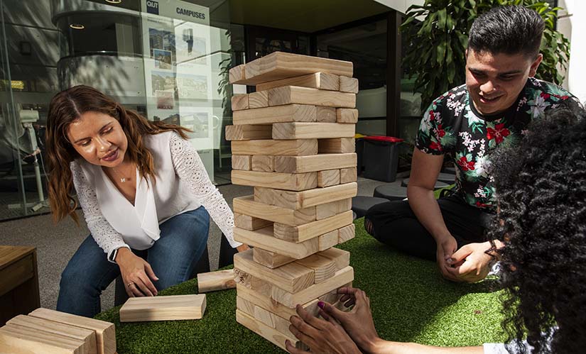 Three students play with a giant set of jenga wooden blocks.
