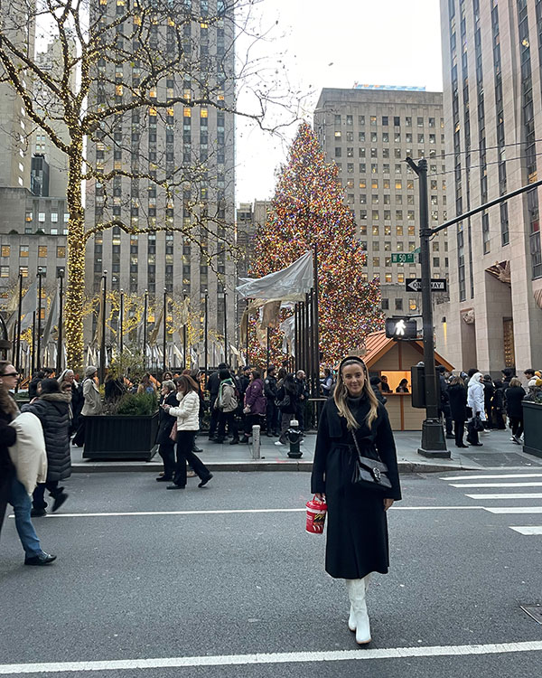 Paige standing in a busy square in New York with a Christmas tree in the background