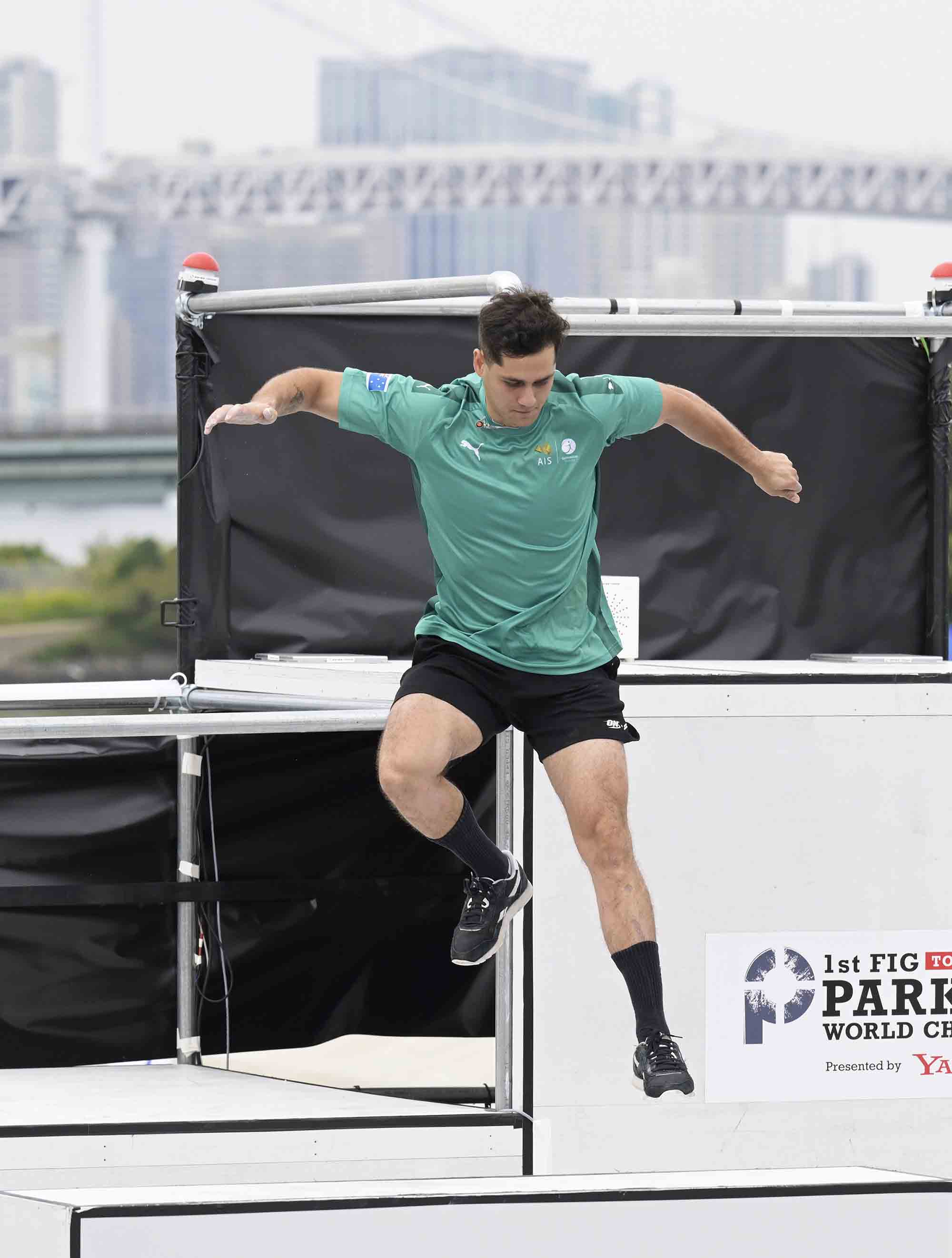 A male in street clothes and sneakers leaps from high ledge in a competition obstacle course.
