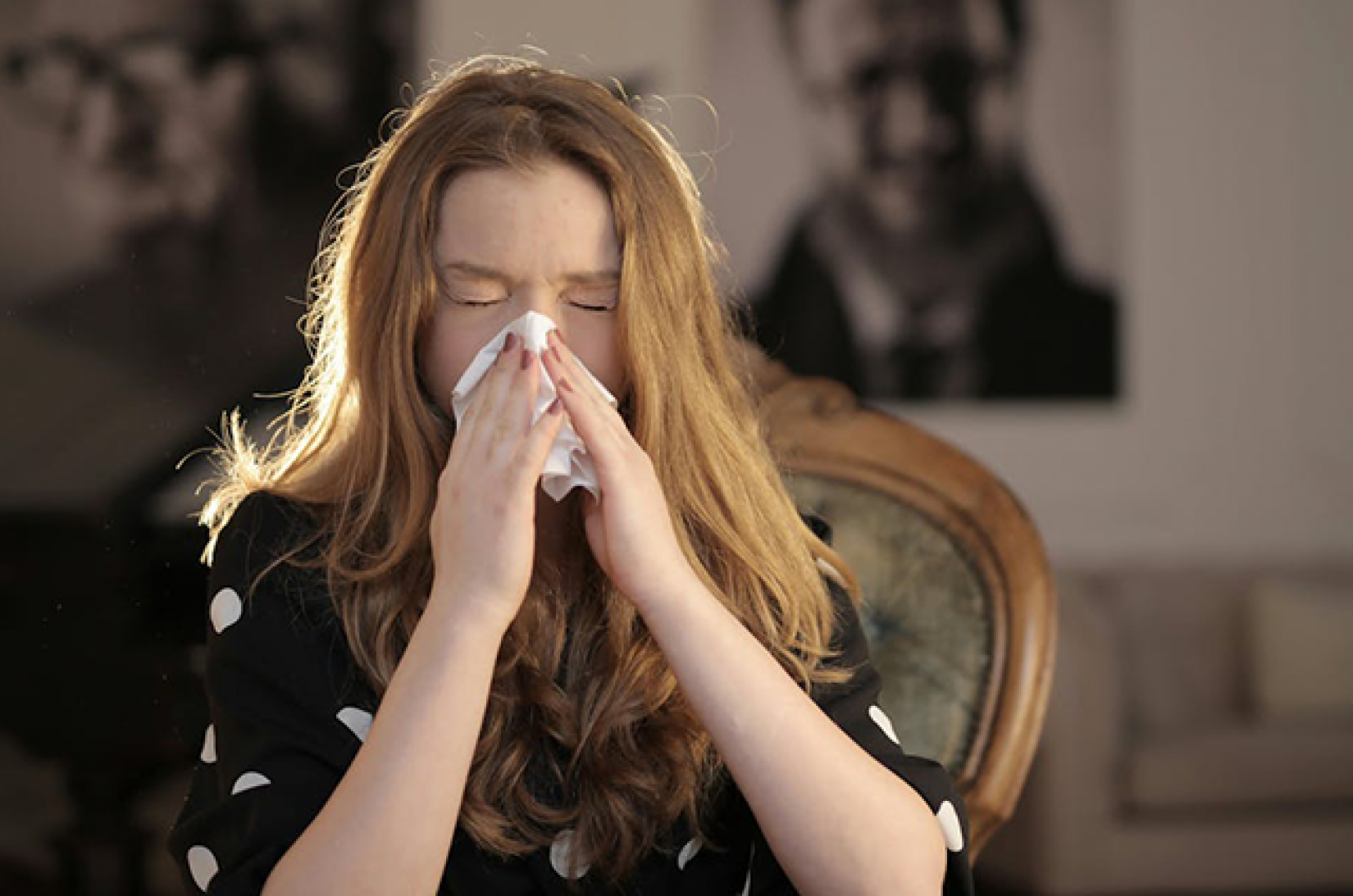 A young woman blowing her nose with a tissue and her eyes closed