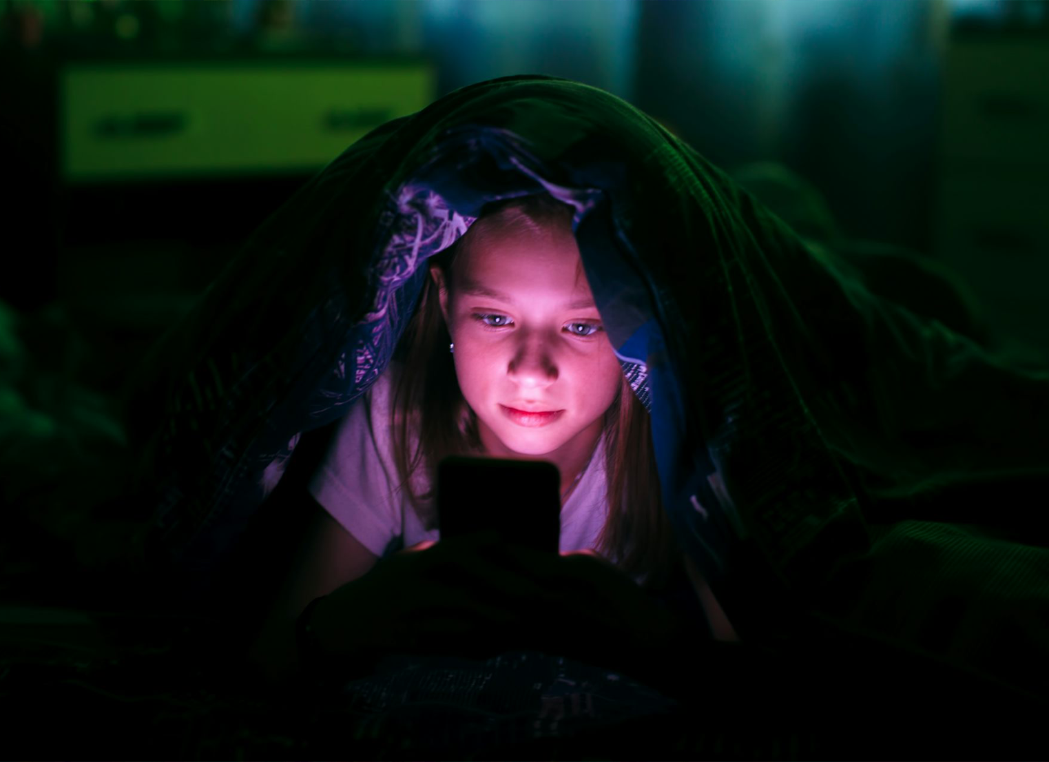 Young girl looking at her phone in the dark under a blanket