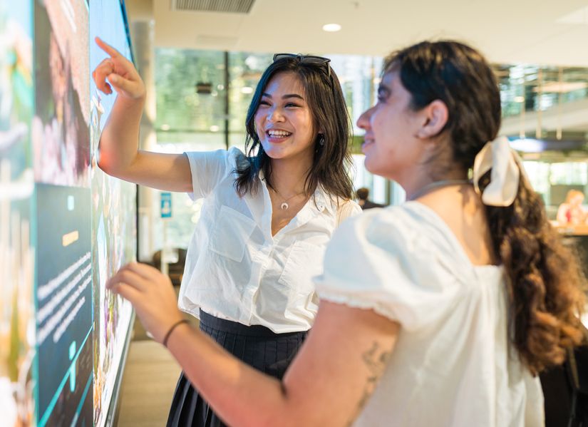 You young smiling women interacting with data science visualisations on a large screen.