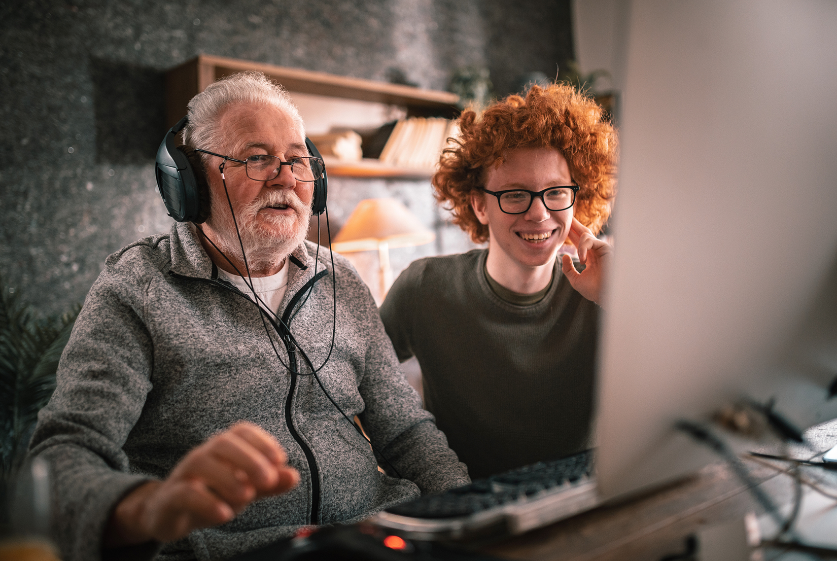 Teenage boy and older man wearing headphones at computer