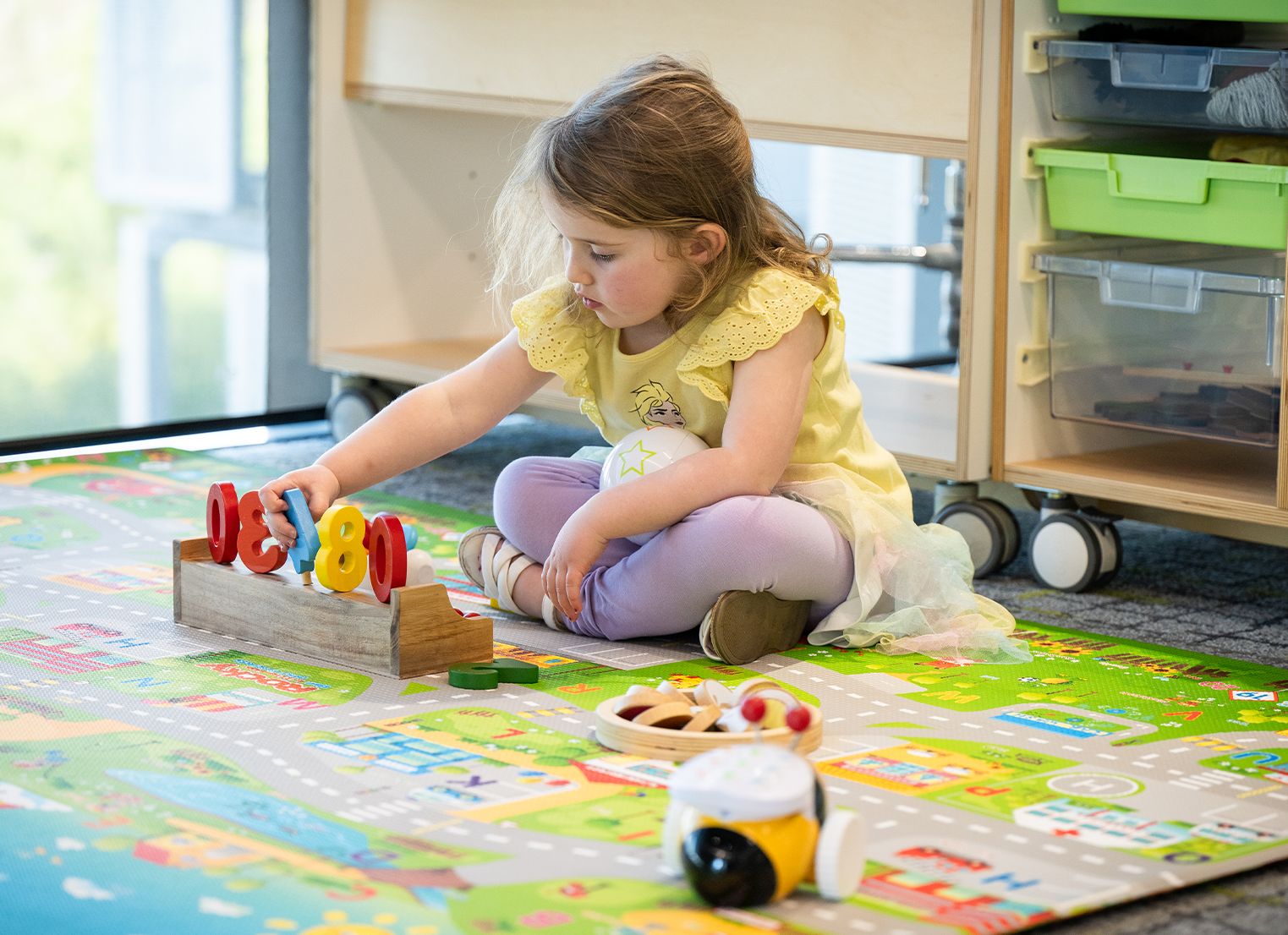 Young girl sits playing with educational toys on a playmat.