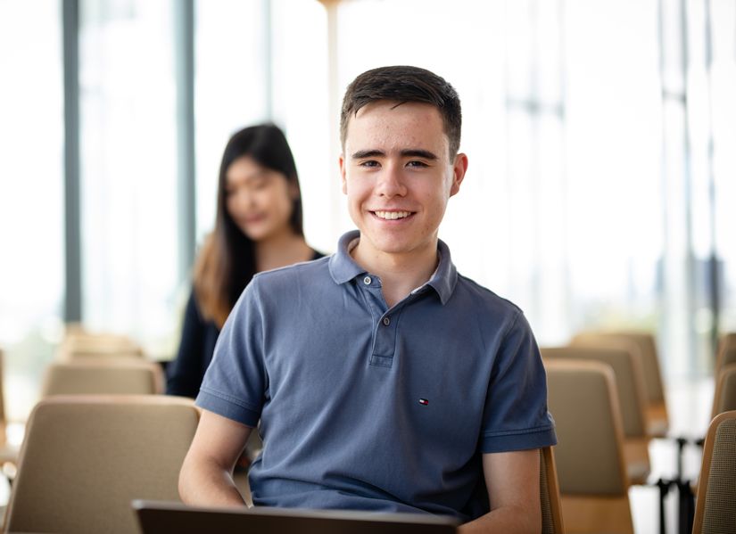 Engineering and Information Technology student Joshua sitting in a bright indoor space, smiling towards the camera with a laptop on his knees